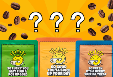 Three mystery coffee bag packages in green, orange, and blue are lined up against a bright yellow background with floating coffee beans and three large question marks above them. The packages feature a smiling coffee cup logo and text including 'SO LUCKY YOU MAY FIND A POT OF GOLD', 'SO GOOD YOU'LL SPICE UP YOUR DAY', and 'SO FRESH IT'S A BERRY SPECIAL TREAT'.