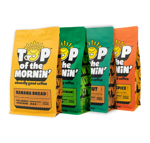 Four stand-up coffee bags from TOP of the MORNIN' arranged side by side on a white background. The bags are in different flavors: yellow (Banana Bread), green (Chocolate Irish Cream), dark green (Hazelnut), and orange (Pumpkin Spice).