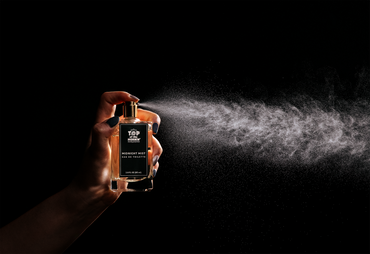 Perfume spray being released from a bottle labeled 'Top Secret' on a black background
